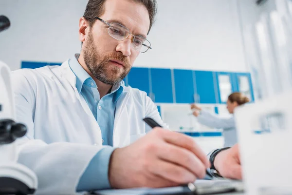 Selective Focus Scientist White Coat Eyeglasses Making Notes Notepad Workplace — Stock Photo, Image