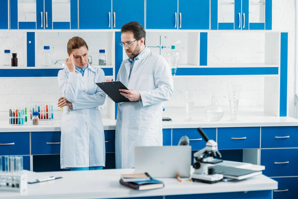 scientific researchers in white coats and eyeglasses with notepad in laboratory