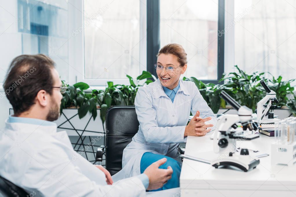 scientists in lab coats and eyeglasses discussing work at workplace in lab