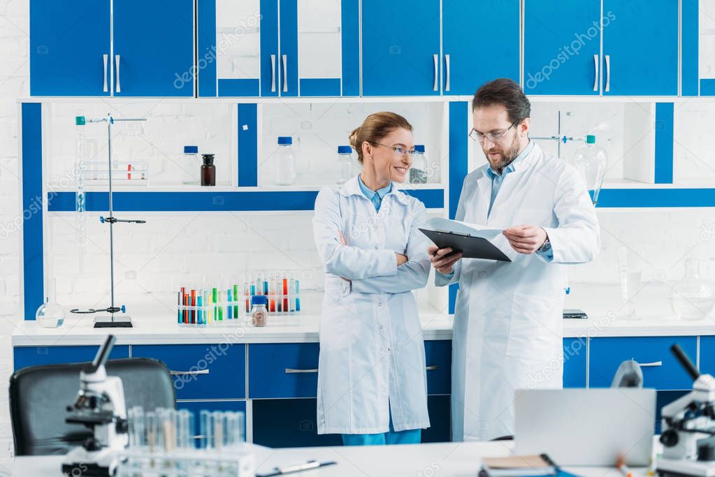 scientific researchers in white coats and eyeglasses with notepad in laboratory