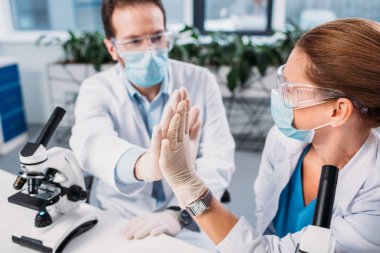 bilim adamları beyaz kat olarak, tıbbi maskeleri ve birbirlerine beşlik laboratuarında vererek koruyucu gözlük