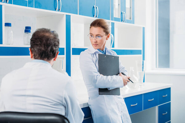 partial view of female scientist with notepad in hands standing near colleague in lab