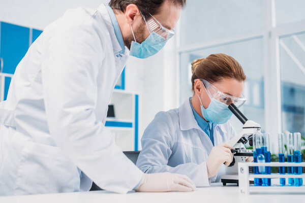 researchers in white coats and medical masks working with reagents together in lab