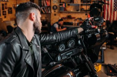 stylish young man in leather on bike at garage clipart