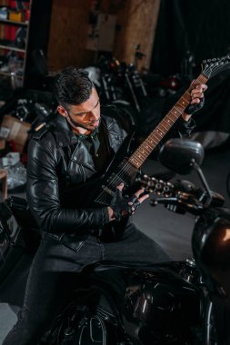 Bisiklet Garage otururken gitar çalmak yakışıklı genç adam
