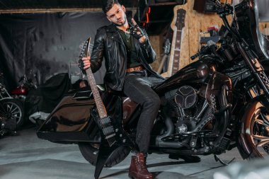 Bisiklet elektro gitar ile garajda otururken deri ceket şık genç adam