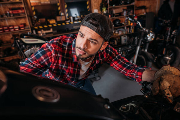 close-up shot of handsome bike repair station worker looking at motorcycle at garage
