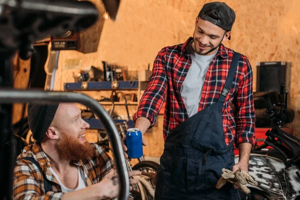 Young Mechanic Passing Canned Drink His Colleague Garage — Stock Photo, Image