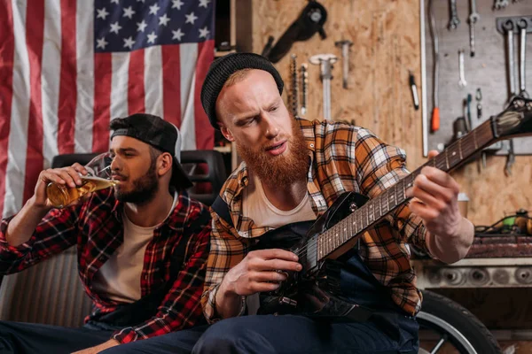 Handsome Mechanics Playing Guitar Drinking Beer Garage — Free Stock Photo