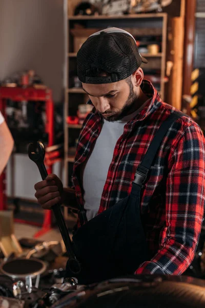 handsome bike repair station worker using wrench at garage