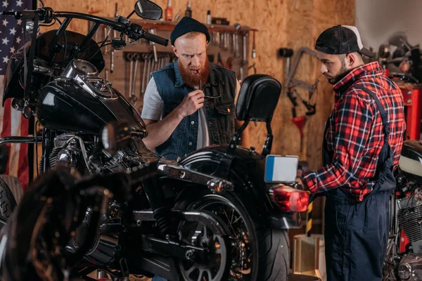 repair worker talking to serious customer near motorcycle at garage