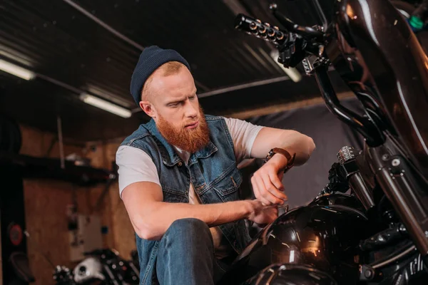 Young Man Looking Watch While Sitting Motorcycle Garage — Free Stock Photo