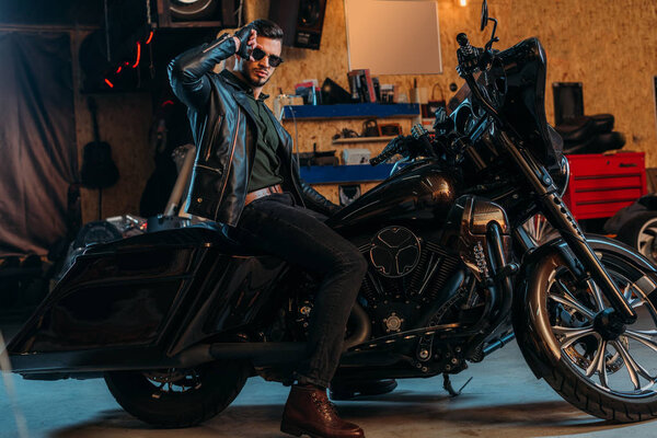 handsome young man in sunglasses sitting on bike at garage