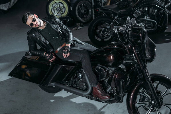 high angle view of handsome young man in leather jacket lying on bike at garage