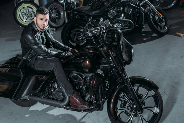 high angle view of handsome young man in leather jacket sitting on bike at garage