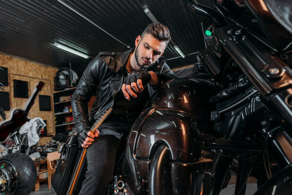 handsome young man sitting on bike with guitar at garage