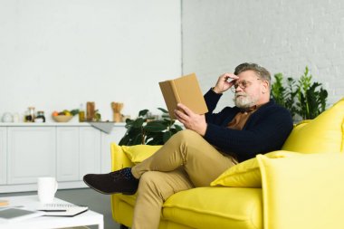 Komuta sizde sarı kanepede oturan ve kitap okuma gözlük sakallı 