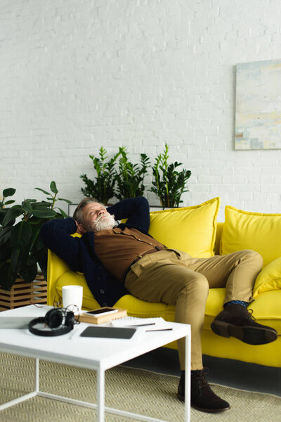 стильный старший мужчина лежит на диване с руками за головой и глядя вверх
