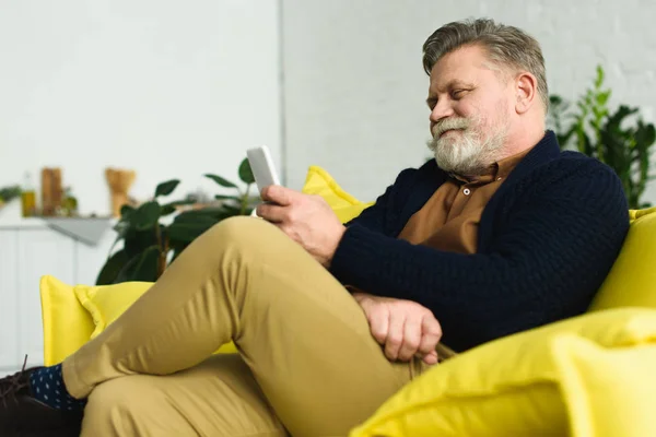 Χαμογελώντας Γενειοφόρος Ανώτερος Άνθρωπος Κάθεται Στον Καναπέ Και Χρησιμοποιώντας Smartphone — Φωτογραφία Αρχείου