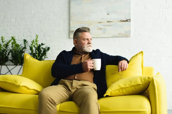 Pensive Senior Man Holding Cup Coffee Sitting Yellow Couch Home — Stock Photo, Image