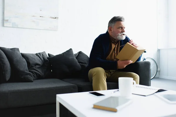 Nadenkend Bebaarde Senior Man Boek Houden Thuis Weg Zoek — Stockfoto