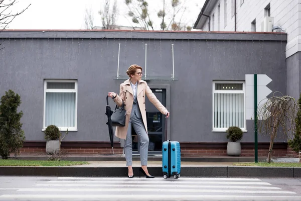 Geschäftsfrau Mit Koffer Und Regenschirm Wartet Auf Der Straße Auf — kostenloses Stockfoto