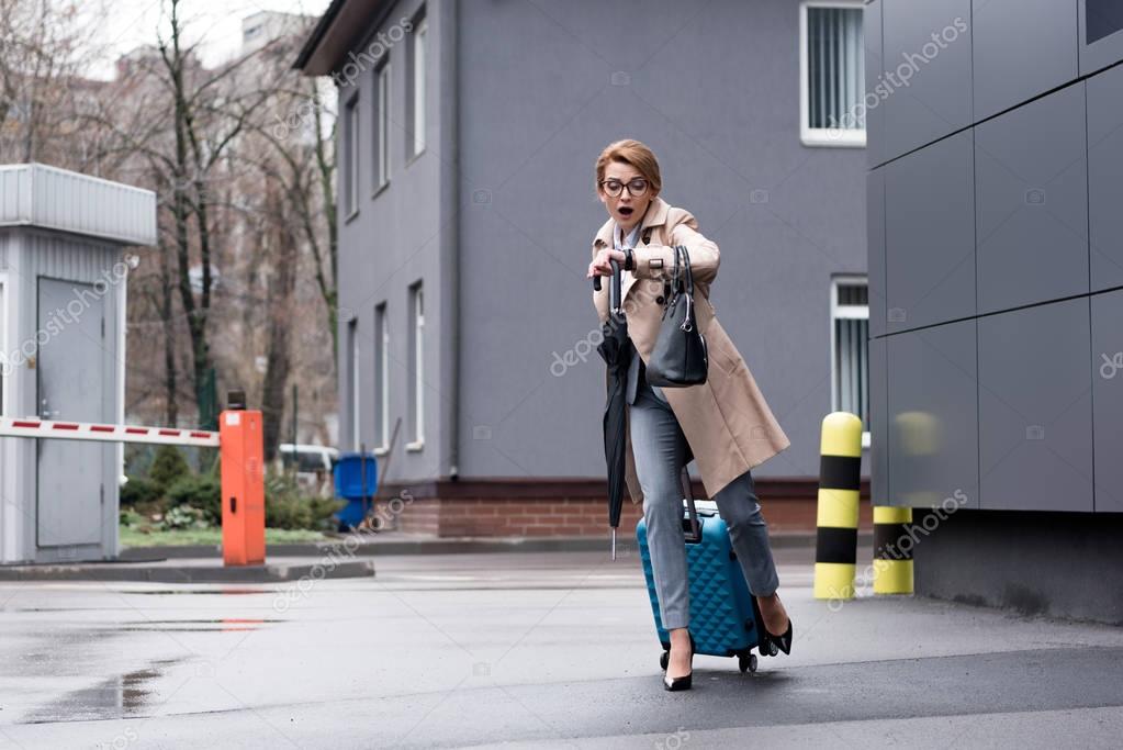 Hurrying businesswoman with suitcase checking time and running on street