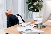 Müde Geschäftsfrau im Anzug am Arbeitsplatz mit Dokumenten im Büro