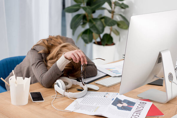 partial view of exhausted businesswoman sleeping at workplace with documents in office