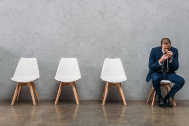 lonely businessman with drug addiction sniffing cocaine while sitting on chair under concrete wall clipart