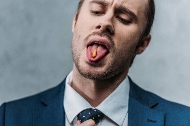 close-up portrait of addicted businessman sticking out tongue with drug pill clipart