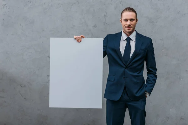 Joven Hombre Negocios Sonriente Sosteniendo Tablero Blanco Frente Pared Hormigón — Foto de Stock