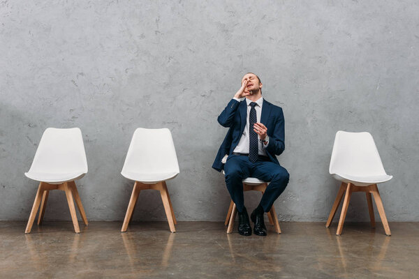 businessman with drug addiction sniffing cocaine while sitting on chair under concrete wall