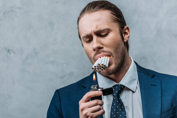 cropped shot of businessman with mouth full of cigarettes trying to smoke it
