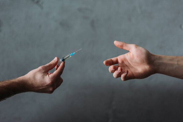 cropped shot of drug dealer giving heroin syringe to person
