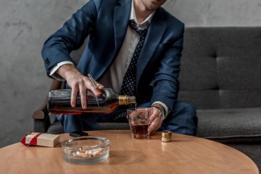 cropped shot of alcohol addicted businessman drinking whiskey while sitting on couch clipart