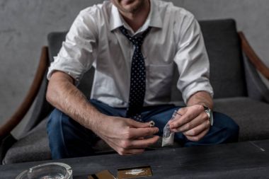cropped shot of businessman with drug addiction holding pack of cocaine clipart