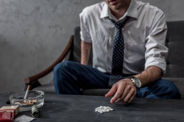 addicted junkie in white shirt and necktie taking mdma pill from table clipart