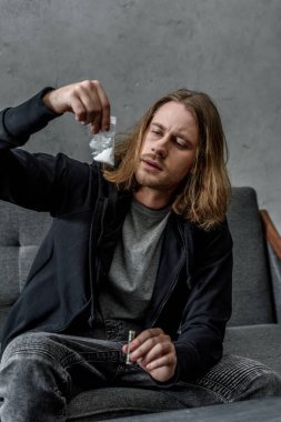 bağımlısı adam kanepede otururken kokain paket üzerinde arıyor