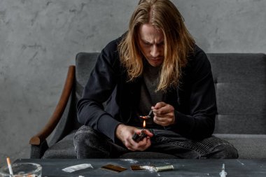 bağımlı keş kanepede otururken çakmak kaşıkla eroin kaynar