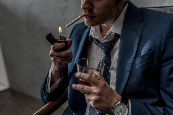 cropped shot of businessman with glass of whiskey smoking cigarette
