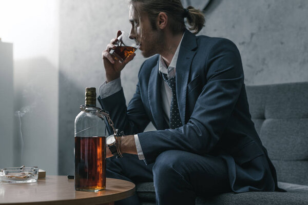 alcohol addicted businessman with glass and bottle of whiskey sitting on couch