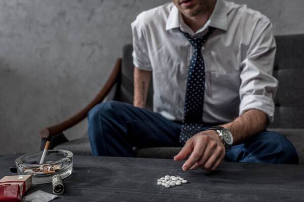 addicted junkie in white shirt and necktie taking mdma pill from table