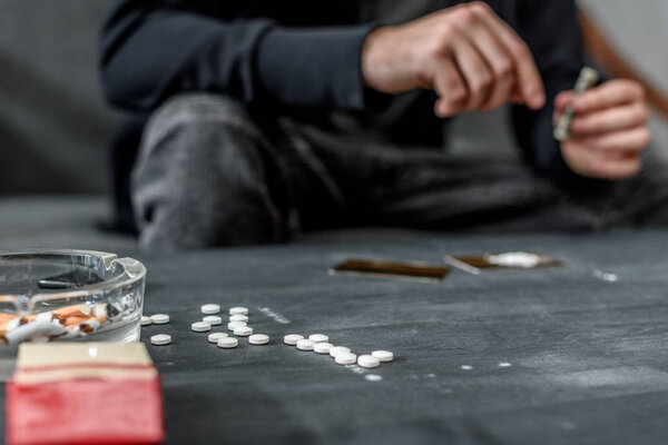 cropped shot of addicted man with various drugs on table