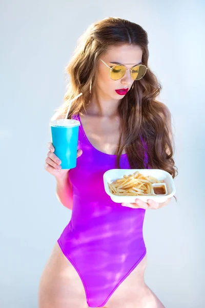 ドリンクを押しながらグレーのフライド ポテトを見て紫水着で超セクシーな魅力的な女の子  — 無料ストックフォト