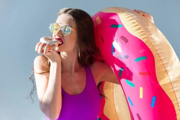 グレーに分離されたドーナツを食べて超紫水着でセクシーな魅力的な女の子 — ストック写真