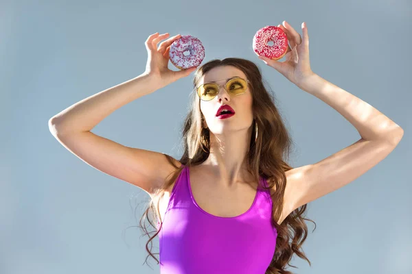sexy attractive girl in ultra violet swimsuit looking at donuts isolated on grey