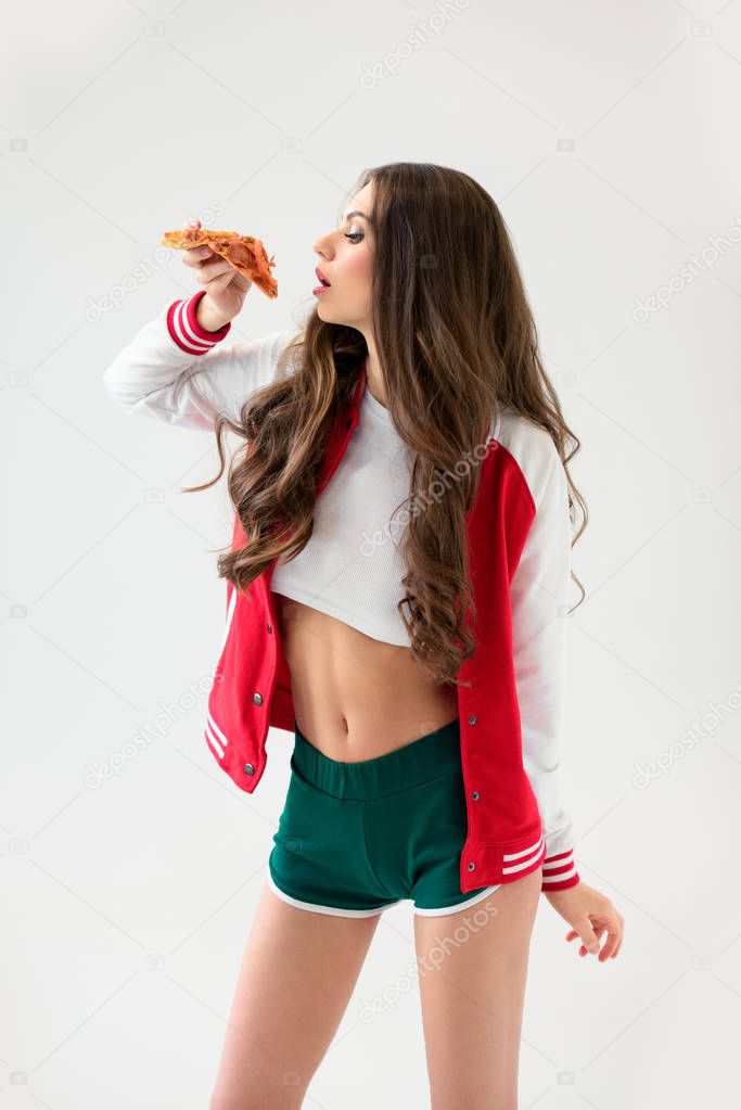 side view of sexy girl in baseball jacket eating pizza isolated on white