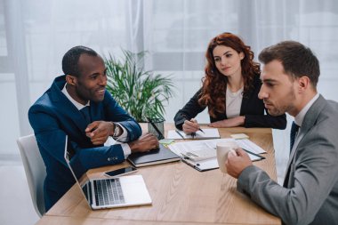 Team of business partners sitting at table with laptop clipart