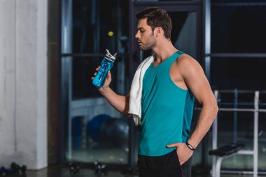 tired sportsman with towel drinking water from sport bottle in gym